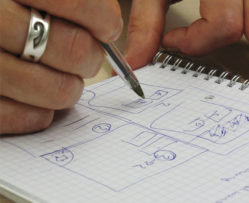 Karierter Block auf dem eine beringte Hand mit Kugelschreiber Sketches zeichnet